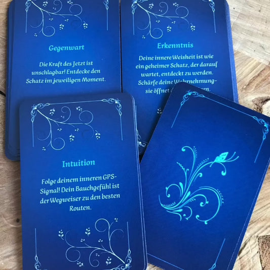 Kartendeck- Achtsame Impulse, Rückseite, blauer Hintergrund mit weißen filigranen Randornamenten und einem Floralem Motiv mit Schmetterling in der Mitte. Vorderseite mit Text und floralen Eckmotiven in weiß.