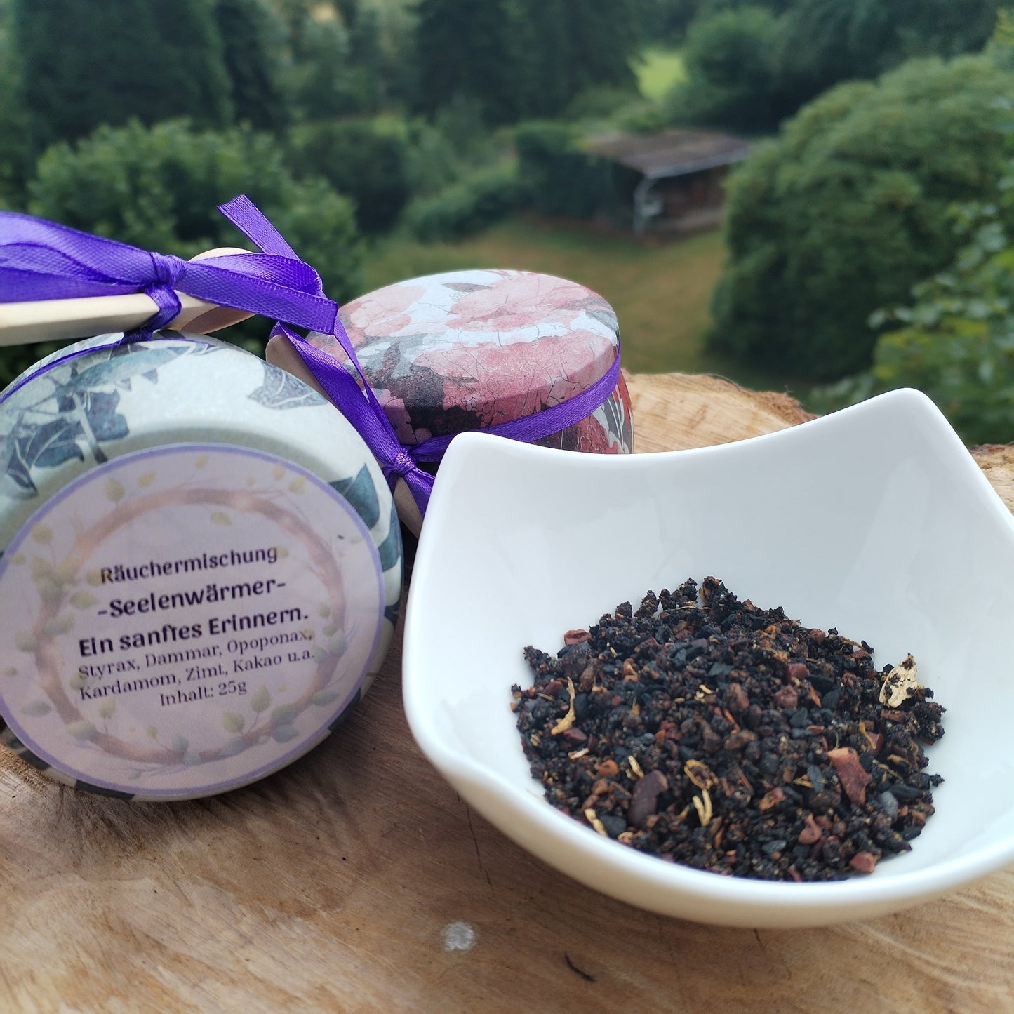 Produkt Räuchermischung Seelenwärmer, abgefüllt in einer bunten Metalldose, die auf einer Holzscheibe steht mit Natur im Hintergrund. Bild 1