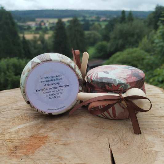 Räuchermischung 'Erinnerung' abgefüllt in einer buntem Metalldose, die auf einer Holzscheibe steht. Im Hintergrund Natur. Produktbild 2