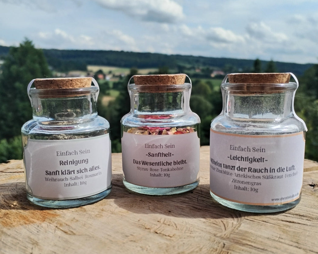 Kollektion Räuchermischungen, 3er Set Einfach sein. 3 Gläser mit Korkstopfen auf einer Holzplatte, im Hintergrund Horizont mit Naturlandschaft.