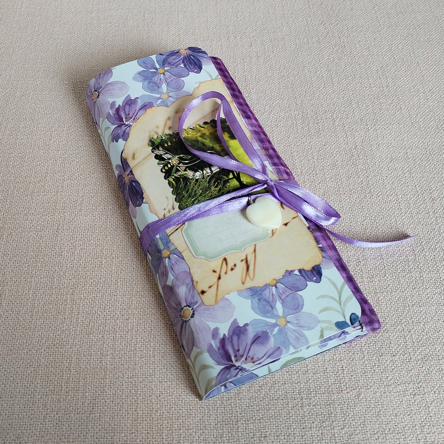 Long-SlimJournal Variante Lila Blumen, Vorderseite mit einem kleinen Kettenanhänger aus Perlmut und einem fliederfarbenem Satinband umwickelt.